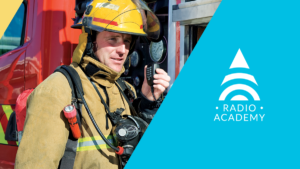 Firefighter holding Tait Mobile Radio system with Tait Radio Academy branding